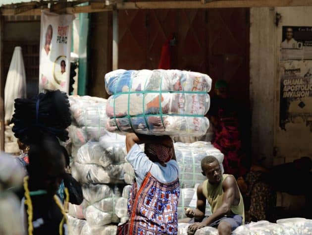 A Kayayei (headporter) transporting a clothing bale from the Importers yard to the main Kantamanto market area during a market day